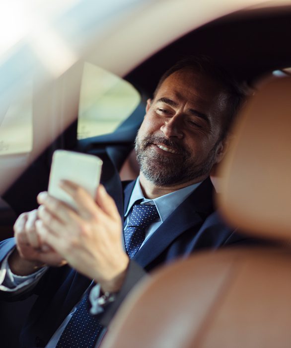 Man in car using smartphone, smiling.